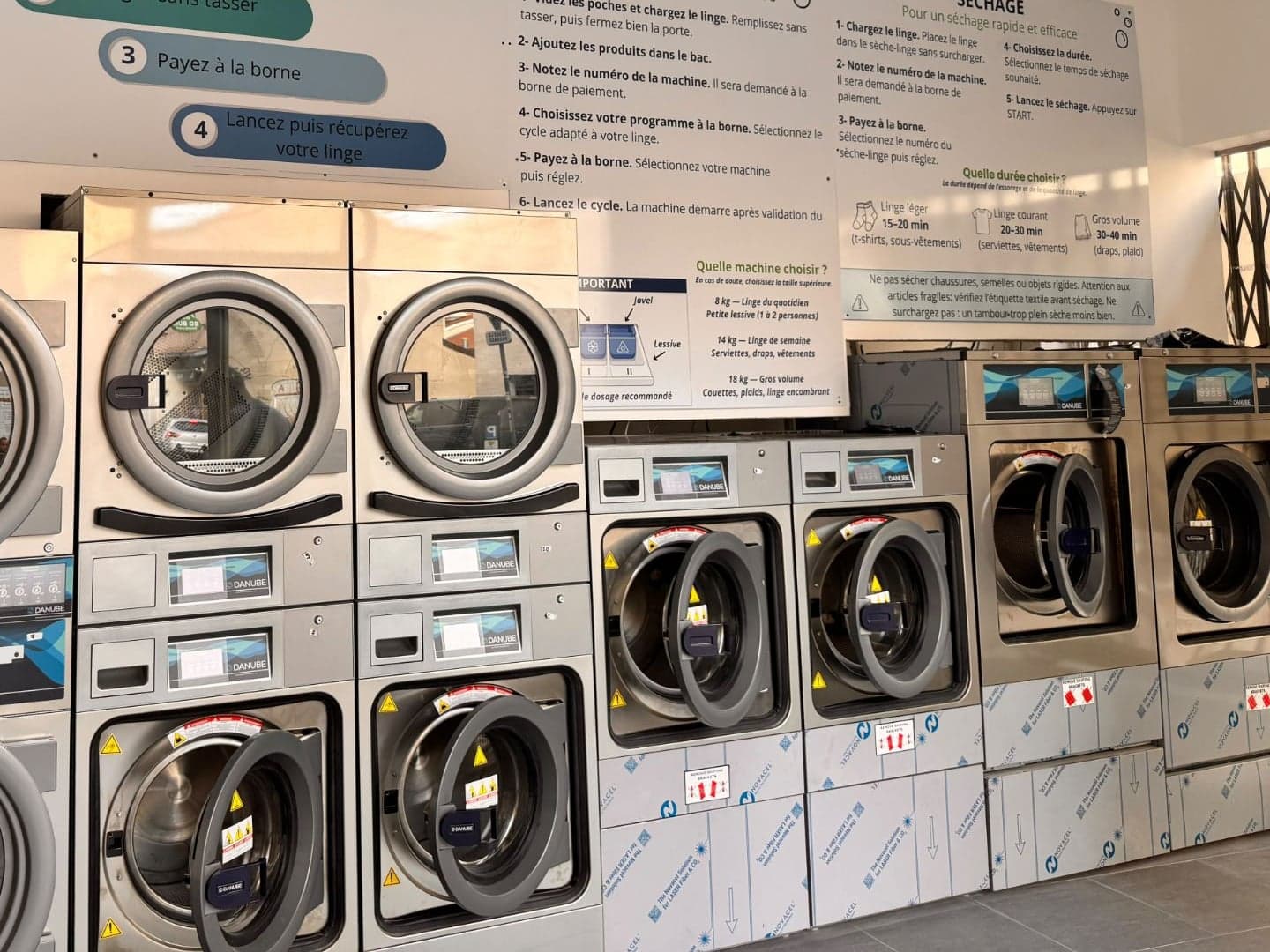 Sèche-linge et machines à laver Green Lavomatic, sous les panneaux d’explication « Lavage » et « Séchage »